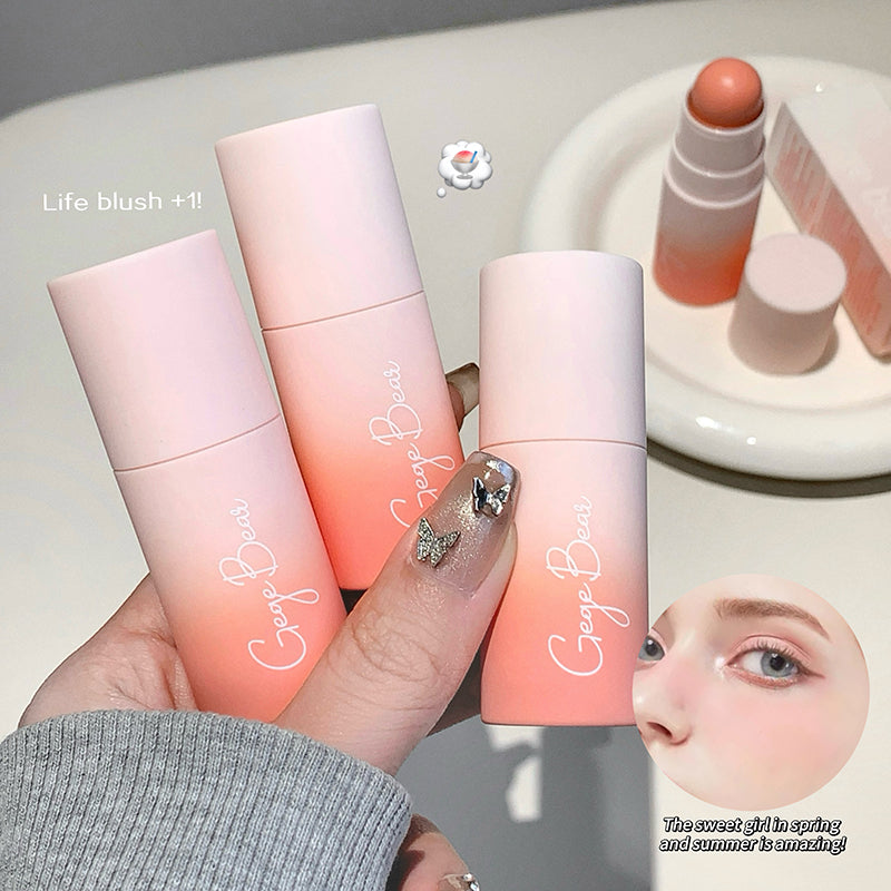 Three pink cosmetic tubes with 'Georg Baer' branding held by a hand, with a blurred face in the corner.