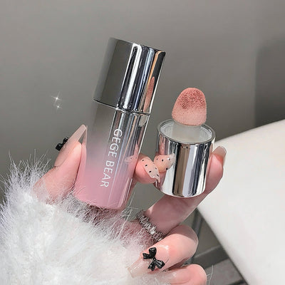 Makeup product with pink cap and silver body held by a hand on a neutral background