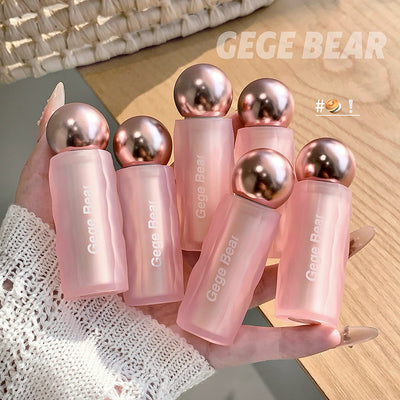 Hand holding pink bottles with metallic caps labeled 'GEGE BEAR' on a wooden surface.