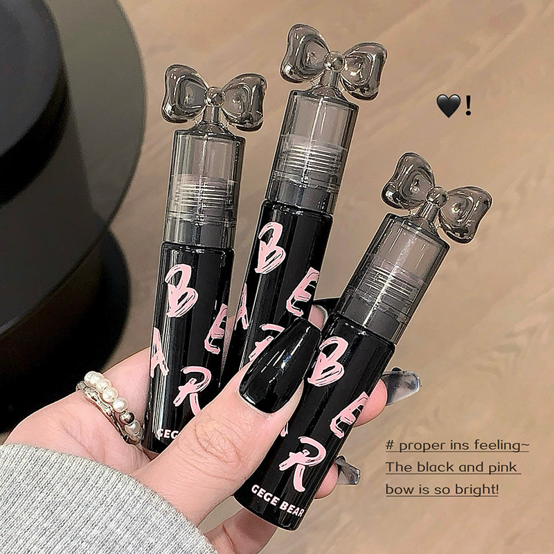 Three black and pink lip glosses with bow designs held by a hand on a beige background.