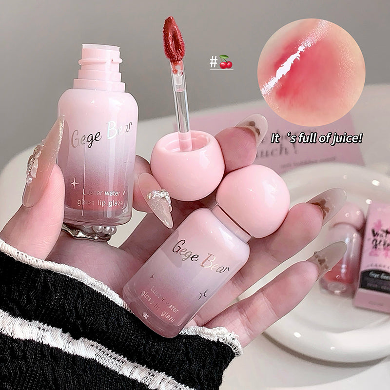 Pink lip gloss set with applicator and bottle held by a hand, with close-up of lip gloss on skin.
