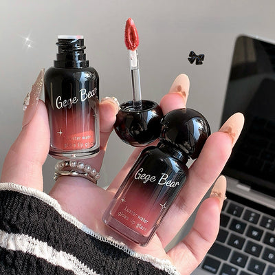 Hand holding two 'Gee Bear' lip products with a blurred laptop background