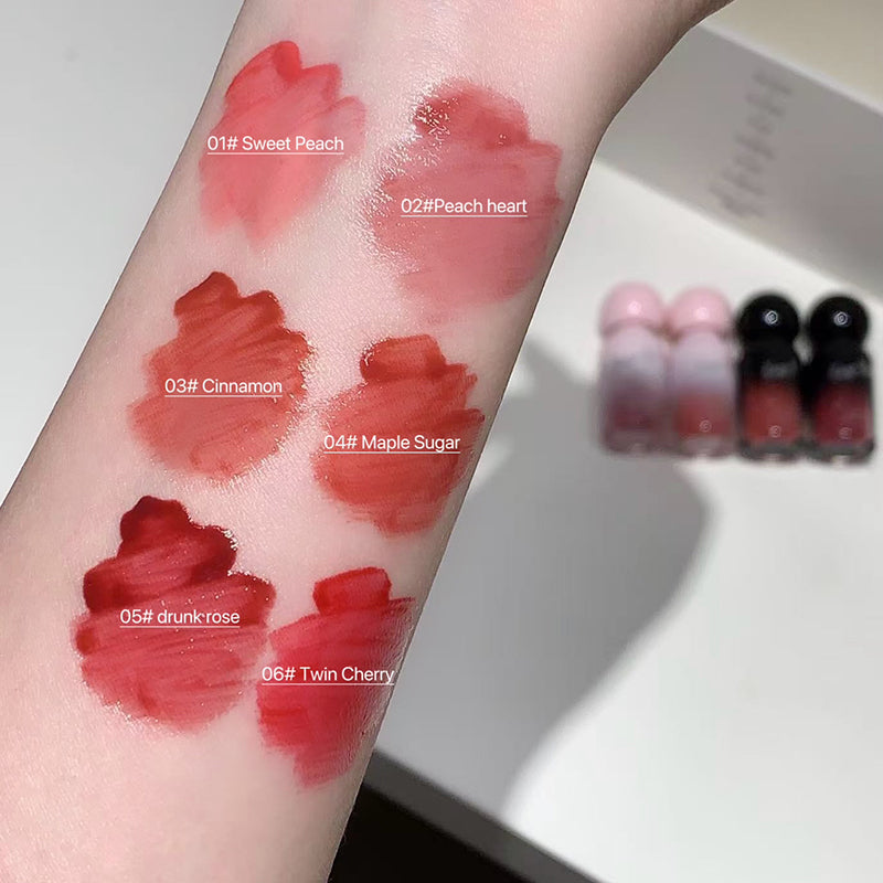 Lipstick swatches on a person's arm with labeled colors and lipsticks in the background.