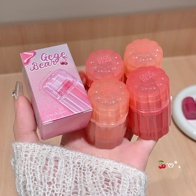 Hand holding Gege Bear lip balm packaging and multiple lip balms on a wooden surface