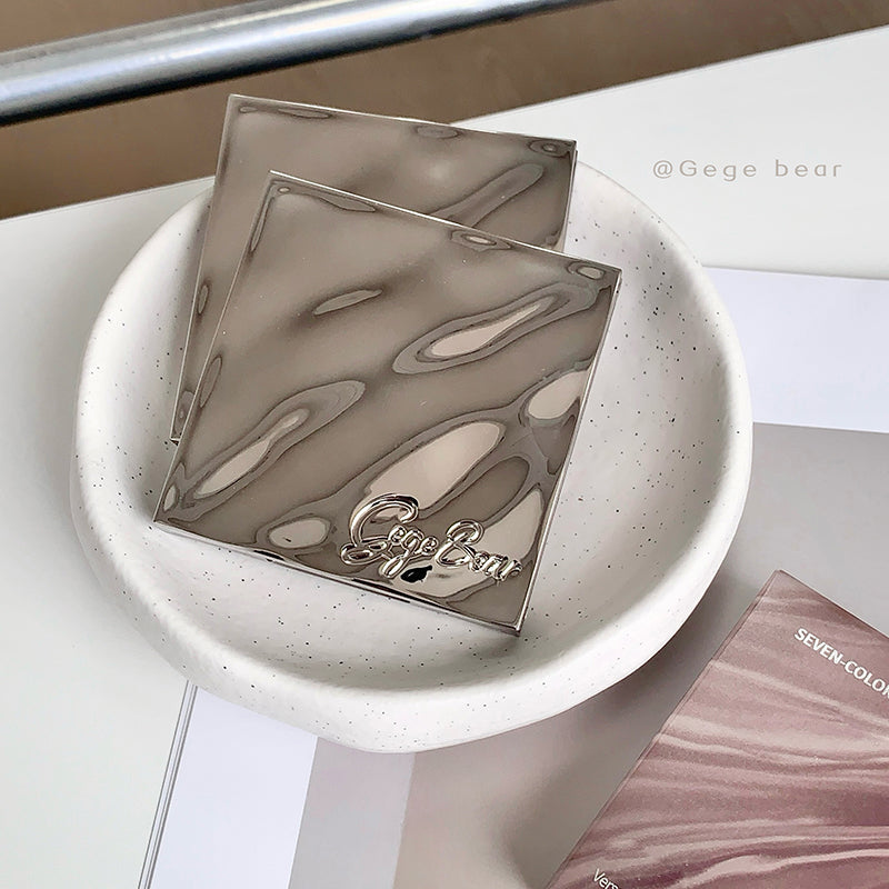 Two metallic compact mirrors on a white dish with 'Gege Bear' branding.