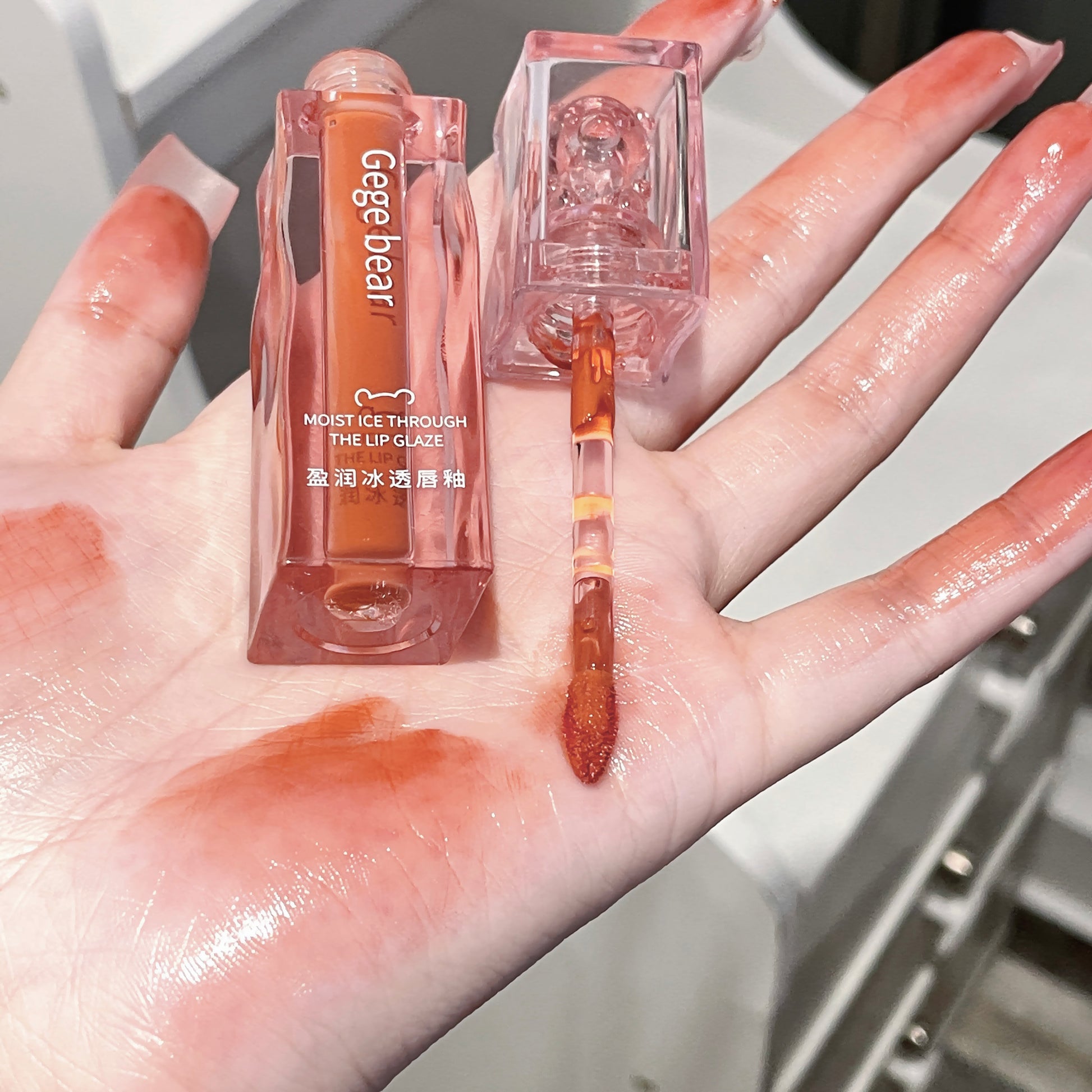 Lip gloss with applicator on a hand, showing color swatch.