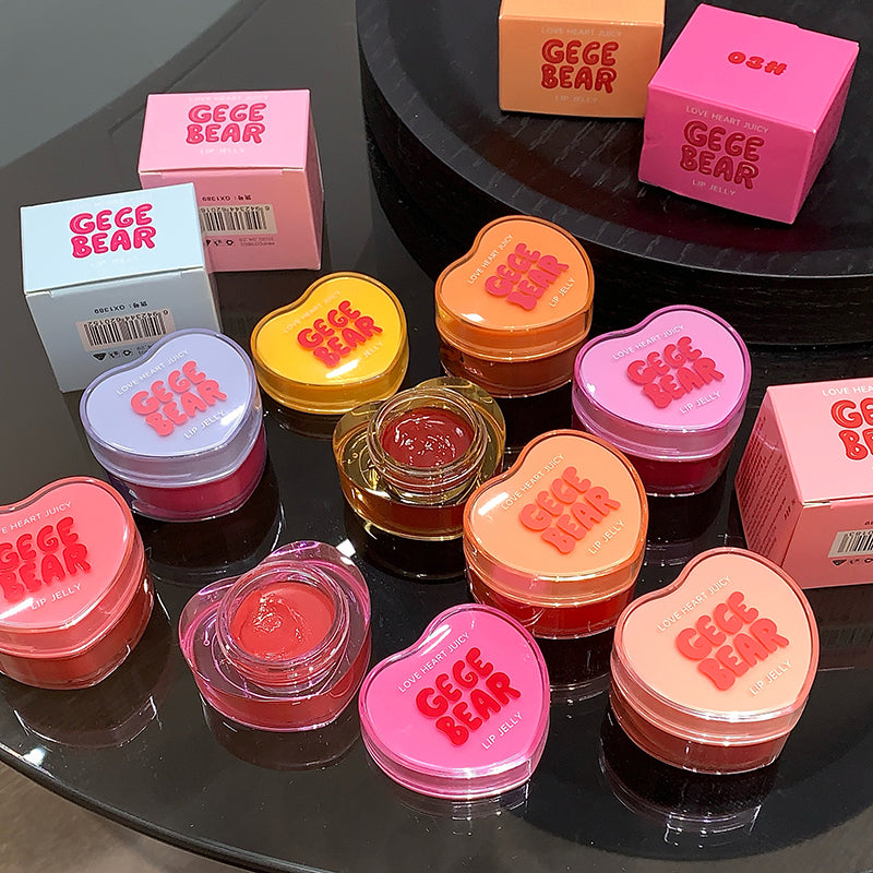Heart-shaped GEGE BEAR lip balm containers on a reflective surface with boxes in the background.