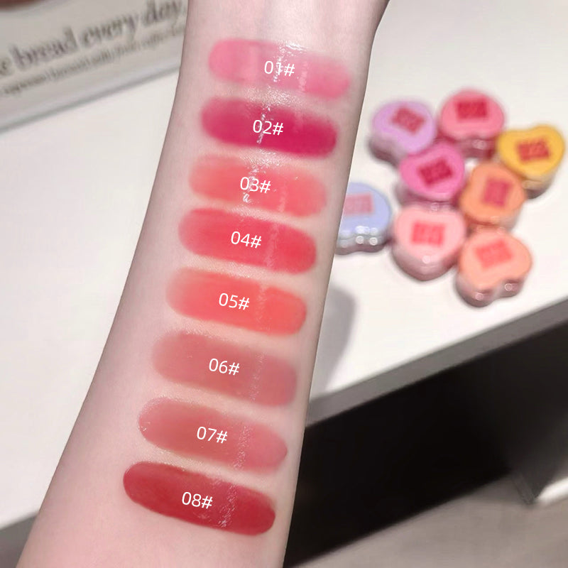 Lipstick swatches on a person's arm with color codes, next to heart-shaped lipsticks.