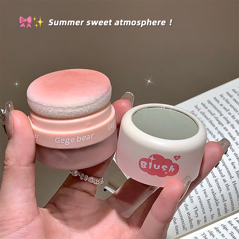 Two small cosmetic containers labeled 'Gege bear' and 'Blush' held by a hand with a blurred background.