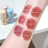 Lipstick swatches on a person's arm with labeled colors and small bottles in the background.