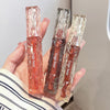 Three Gege Bear lip glosses held in a hand against a neutral background