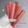 Hand holding multiple Gege bear lip glosses on a gray background