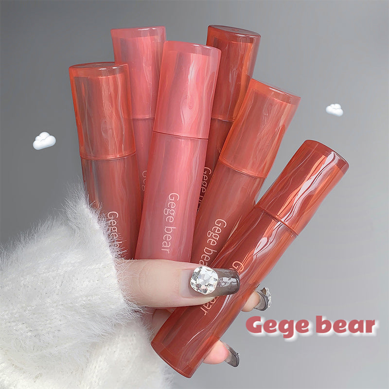 Hand holding multiple Gege bear lip glosses on a gray background
