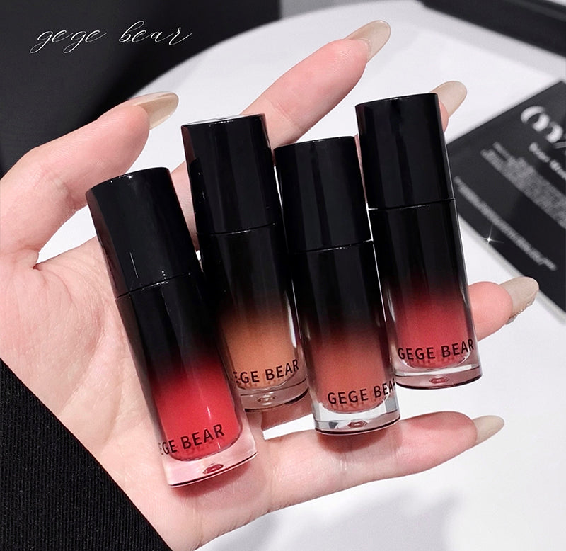 Hand holding four GEGE BEAR lip glosses with gradient colors on a white background