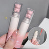 Two pink lip glosses with bear-shaped caps held by a hand, on a gray background.