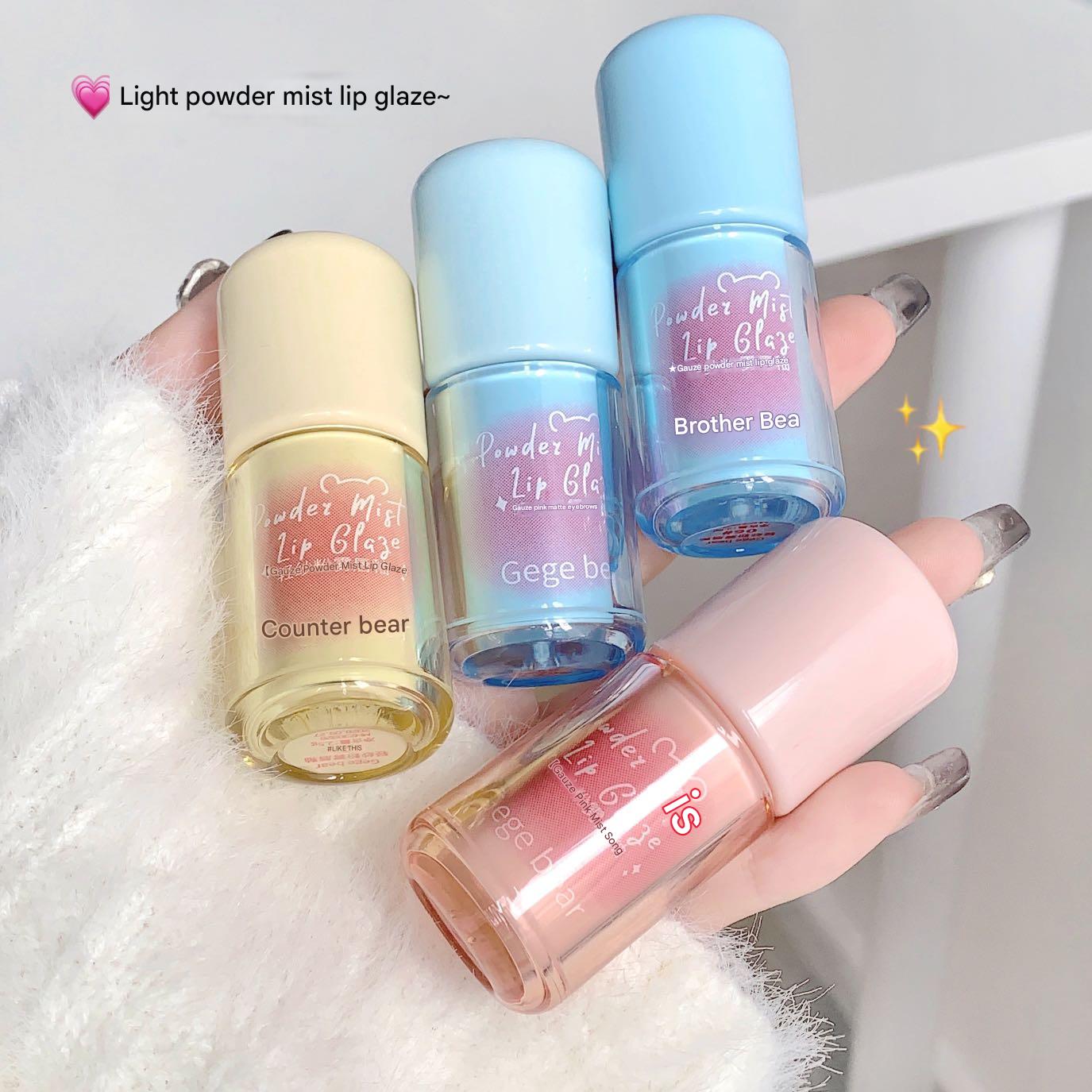 Four light powder mist lip glazes held by a hand on a white background