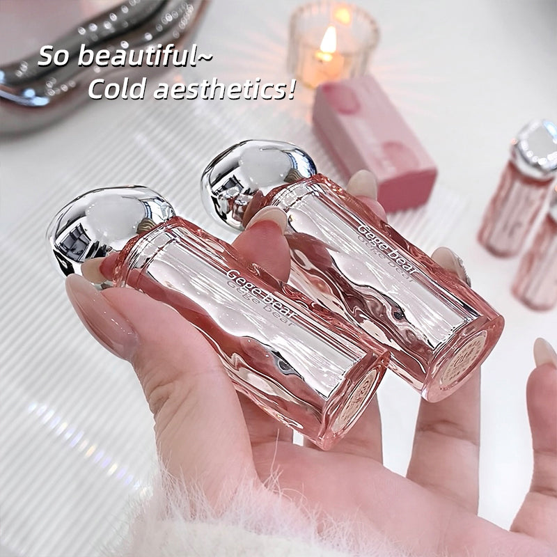 Hand holding a clear perfume bottle with silver cap, surrounded by lip products on a light background.