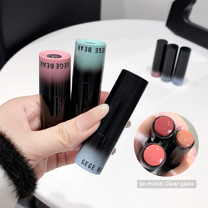 Hand holding a black and gradient-colored lipstick with 'GECE BEAR' branding, surrounded by more lipsticks on a white surface.