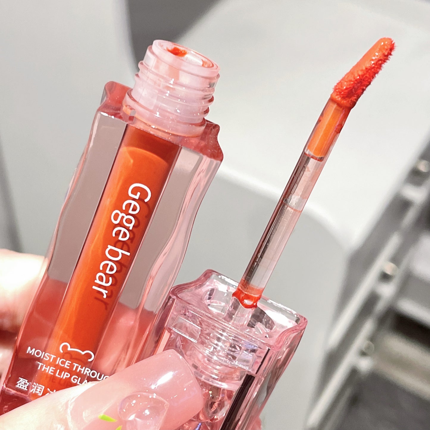 Lip gloss with applicator held by a hand, brand 'Gege bear' visible