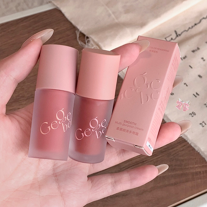 Two pink lip products and their packaging held in a hand on a wooden surface.