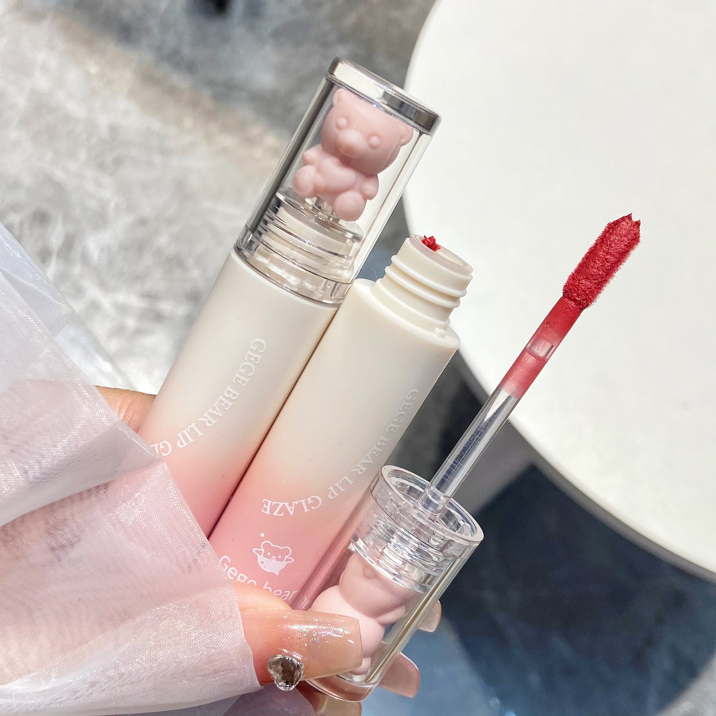 Lip gloss with applicator held by a hand against a neutral background