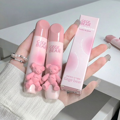Three pink lip glosses with bear designs held by a hand on a white surface.