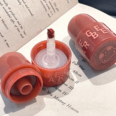 Open coral-colored lip balm with visible brand name on a book page background