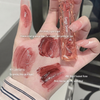 Hand with lipstick swatches and a lip gloss tube labeled 'Geege Bear' on a blurred background