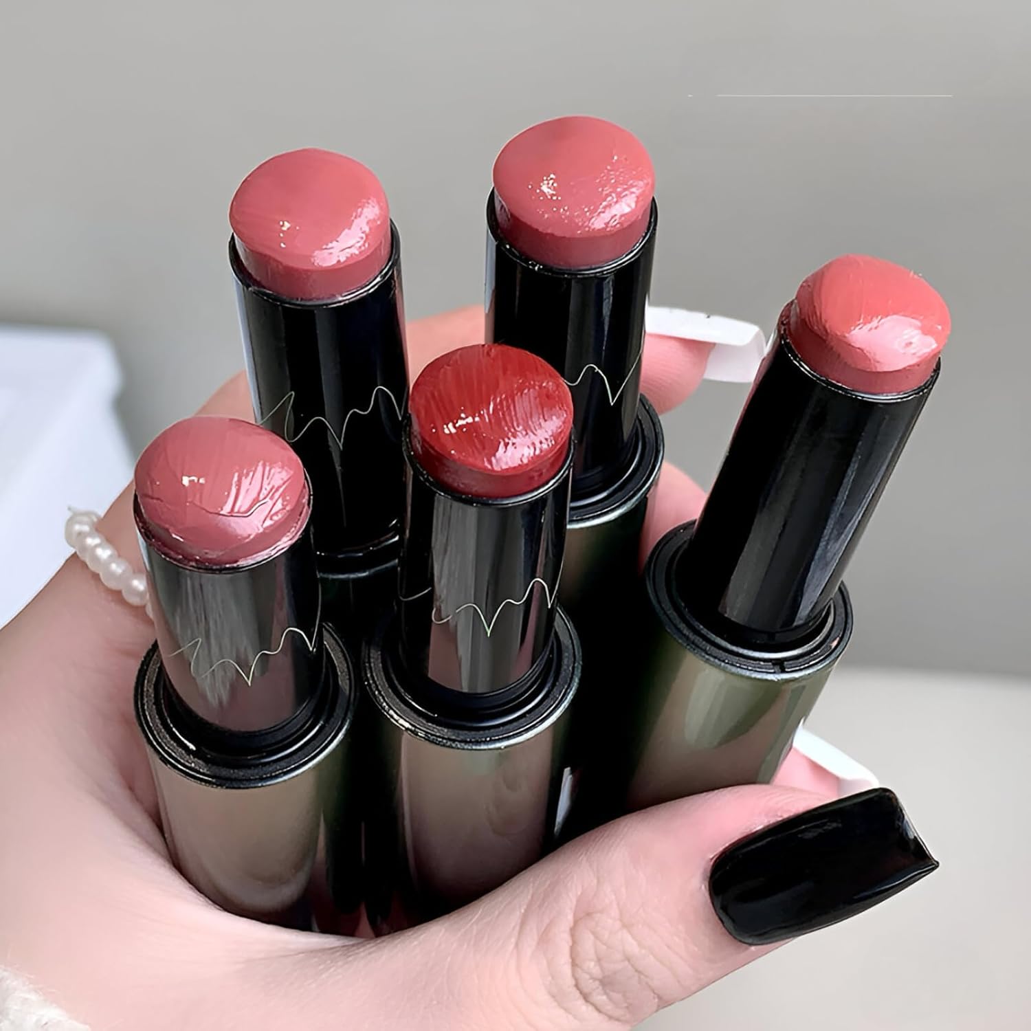 Hand holding six lipsticks with pink shades and black tubes.